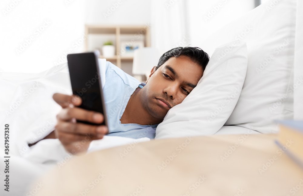 people, bedtime and rest concept - sleepy indian man with smartphone lying in bed at home people, bedtime and rest concept - sleepy indian man with smartphone lying in bed at home