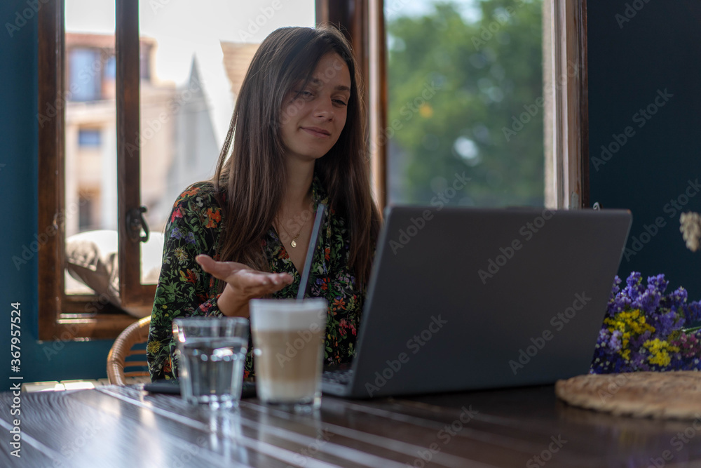 Fototapeta premium Young female using laptop, communicates on internet with customer/colleague coffee mug on table. Cozy office workplace, remote work, E learning concept