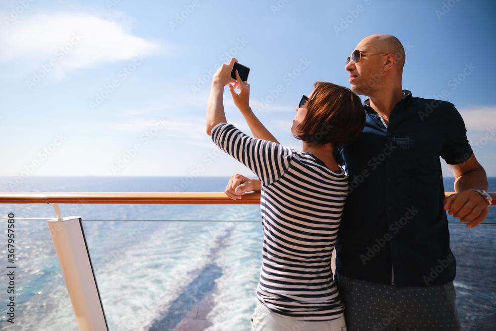 bald man and brunette woman traveling on cruise liner ship and taking pictures from smartphone on balcony 