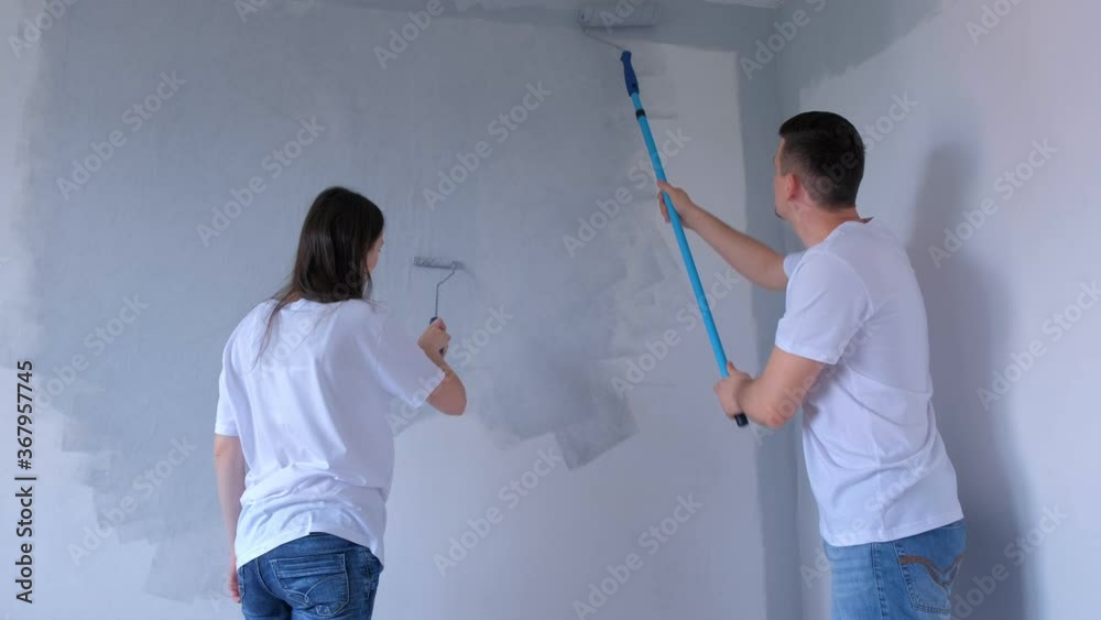 Couple young man and woman are painting wall in gray using paint rollers. Family wife and husband making renovation in new apartment, flat, room. Construction and finishing work in house yourself. Couple young man and woman are painting wall in gray using paint rollers. Family wife and husband making renovation in new apartment, flat, room. Construction and finishing work in house yourself.