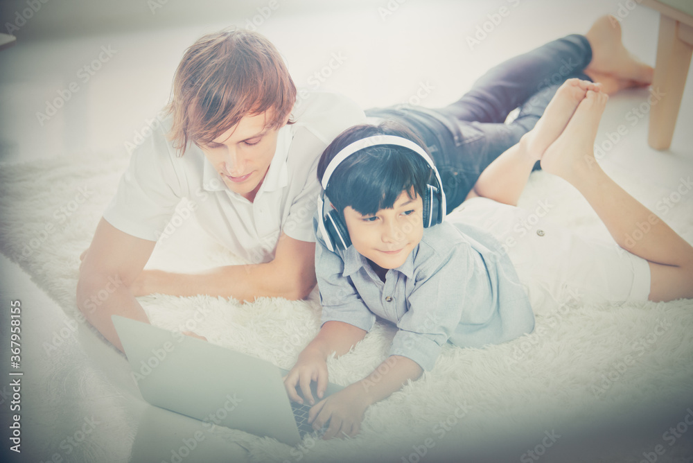 Father and son using laptop while lying on the floor in the living room at home. Vintage tone Father and son using laptop while lying on the floor in the living room at home. Vintage tone