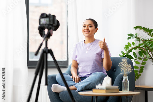 blogging, videoblog and people concept - happy smiling african american female video blogger with camera videoblogging at home and showing thumbs up