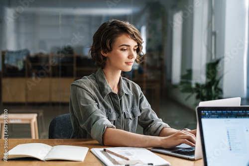 Image of young focused woman working with laptop while sitting at table photo