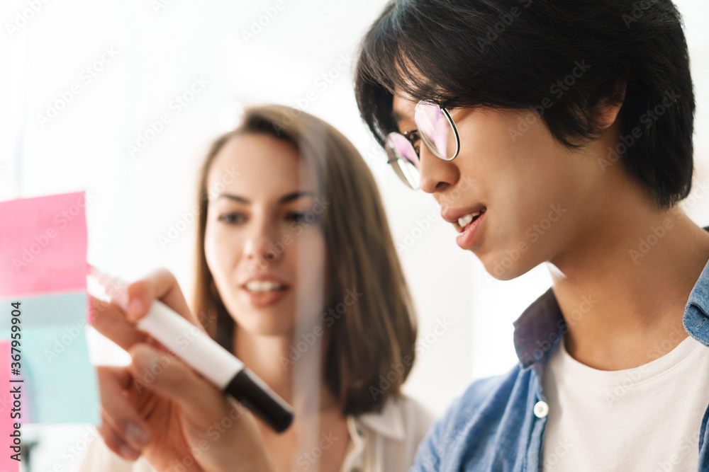 Image of young multinational pleased colleagues using marker pen Image of young multinational pleased colleagues using marker pen