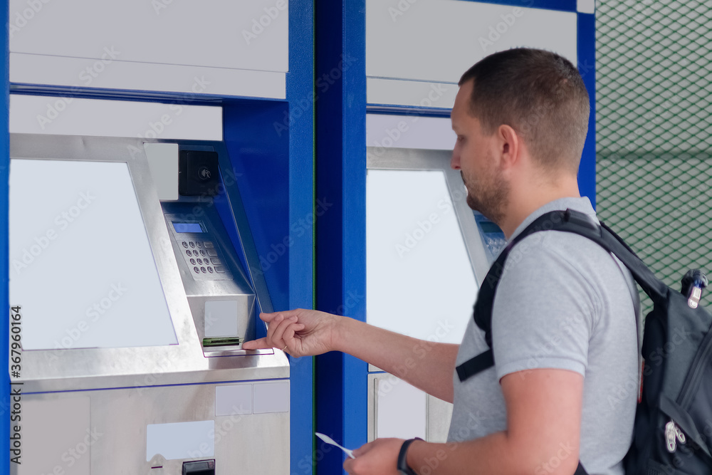 A young man pays for the purchase of a high-speed train ticket at the self-service ticket office in the station building. The concept of online travel