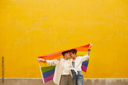 Fotografie Two happy lesbians in love they standing against the yellow wall outdoors and ho