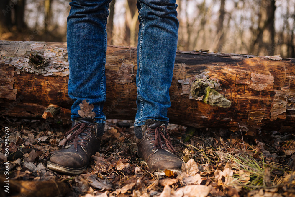 close up photo of human legs in old leather boots and blue jeans standing on the ground with dried leaves close up photo of human legs in old leather boots and blue jeans standing on the ground with dried leaves