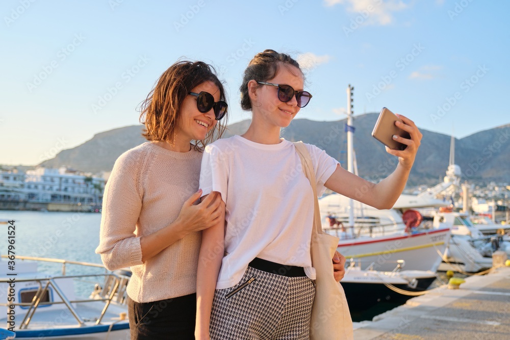 Happy family on vacation, mom and teenage daughter taking selfie on smartphone