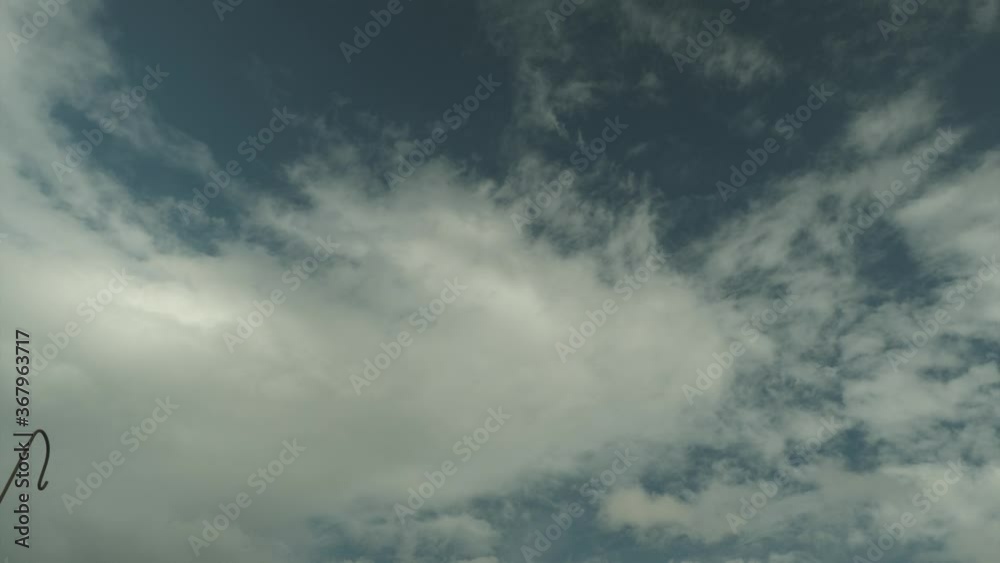 Time lapse: white cumulus and stratus clouds moving fast in blue sky with steel metal single plant shepherd hook in foreground on sunny day, low vantage static Time lapse: white cumulus and stratus clouds moving fast in blue sky with steel metal single plant shepherd hook in foreground on sunny day, low vantage static