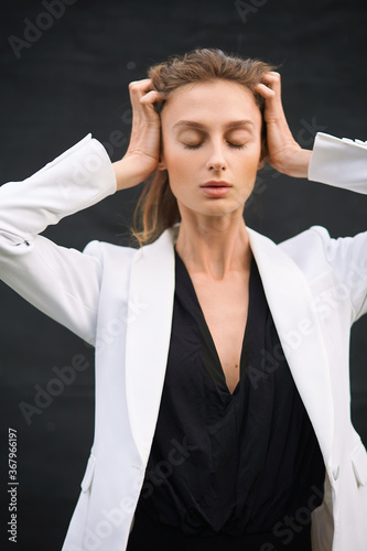 Beautiful yoyng girl is posing outdoors on black canvas. Black bodysuit and white blazer looks. photo