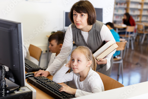 Young female teacher working with schoolgirl in computer class of school library