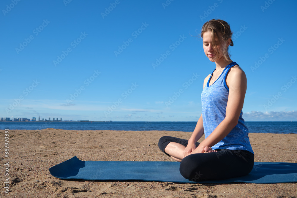Young slender girl doing yoga on the beach on a sunny morning, sad mood, sad thoughts