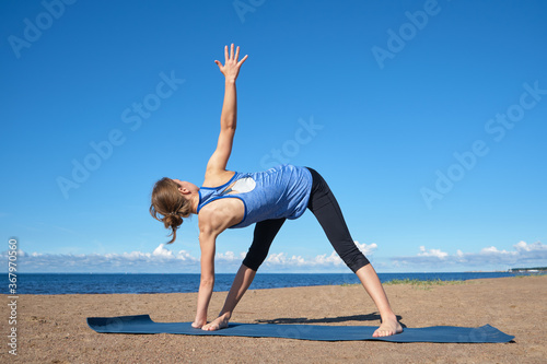 Young slim girl doing yoga on the beach on a sunny morning, stretching before doing sports