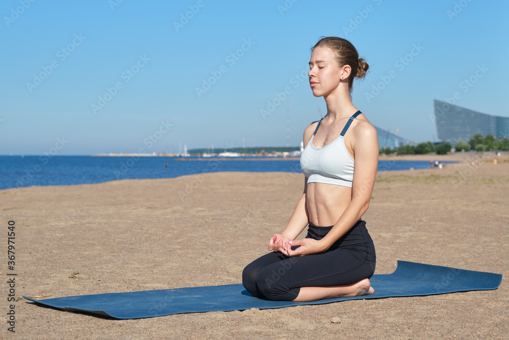 Young slim girl doing yoga, lotus position on the beach, relaxation and meditation