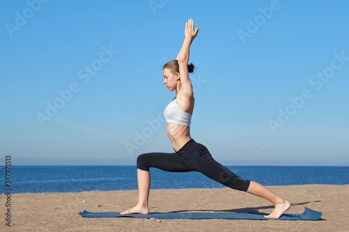 Young slim girl doing yoga on the beach on a sunny morning, stretching before doing sports