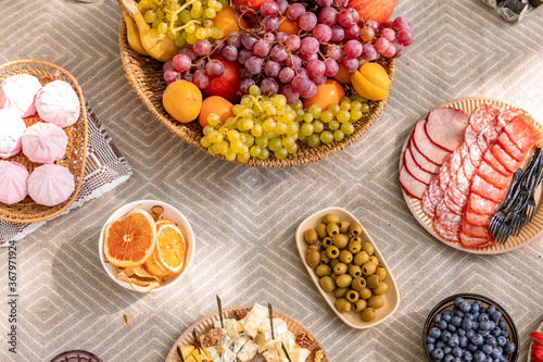 Cutting board with fruits, olives, cold cuts, blueberries, marshmallows, dried orange and cheese platteron. the table is flooded with sunlight