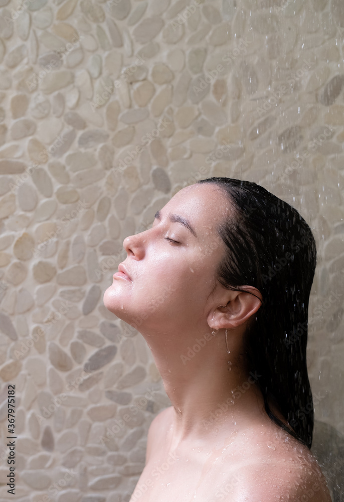 Naklejka premium Close up of slim brunette woman in the shower with light wall background