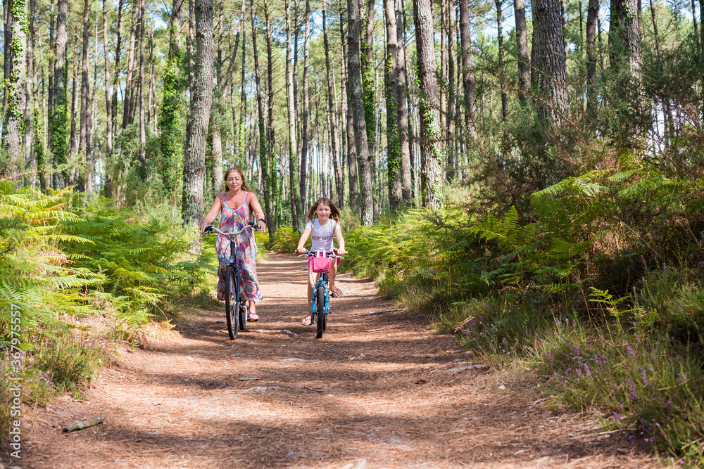 cute little girl and her mom riding a bicycle in a pine forest cute little girl and her mom riding a bicycle in a pine forest