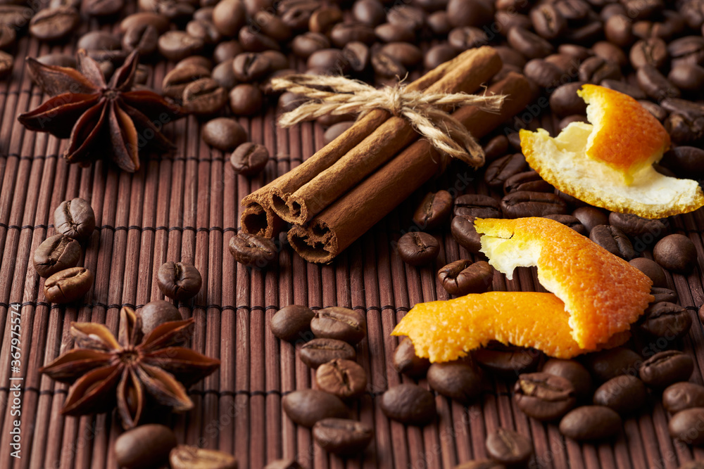 Fototapeta premium Roasted whole coffee beans, tied sticks of cinnamon, anise and orange zest on a dark background