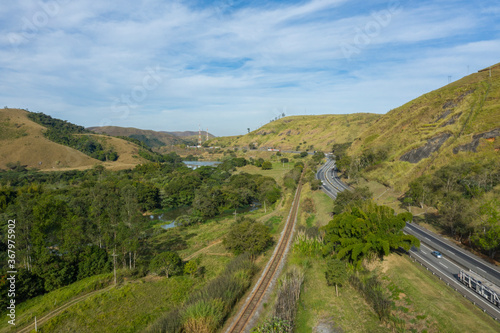 Highway with river and train road. Aerial landscape view of a scenic road in the valley surrounded by the beautiful Brazilian Mountains. 