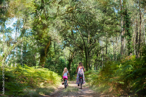 cute little girl and her mom riding a bicycle in a pine forest