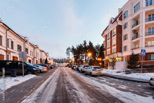 Empty city street, parked cars and road in snow.