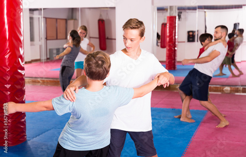Kids with adults practicing effective techniques of self-defence in training room