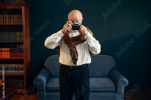 Elderly writer holds retro photo camera in office