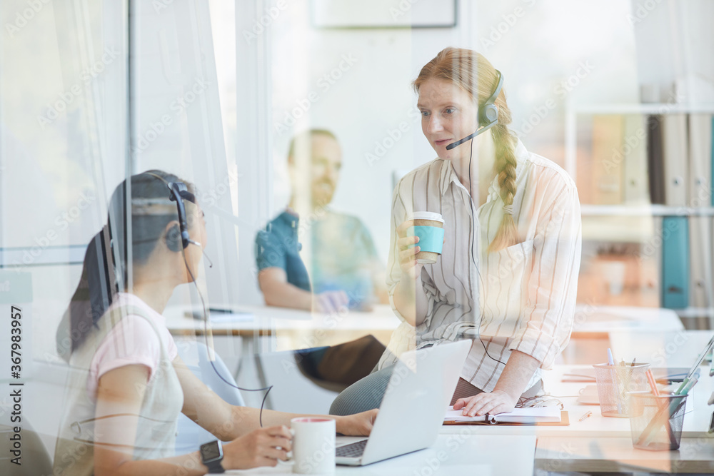 Two businesswomen have coffee break at office they talking to each other behind the glass wall Two businesswomen have coffee break at office they talking to each other behind the glass wall