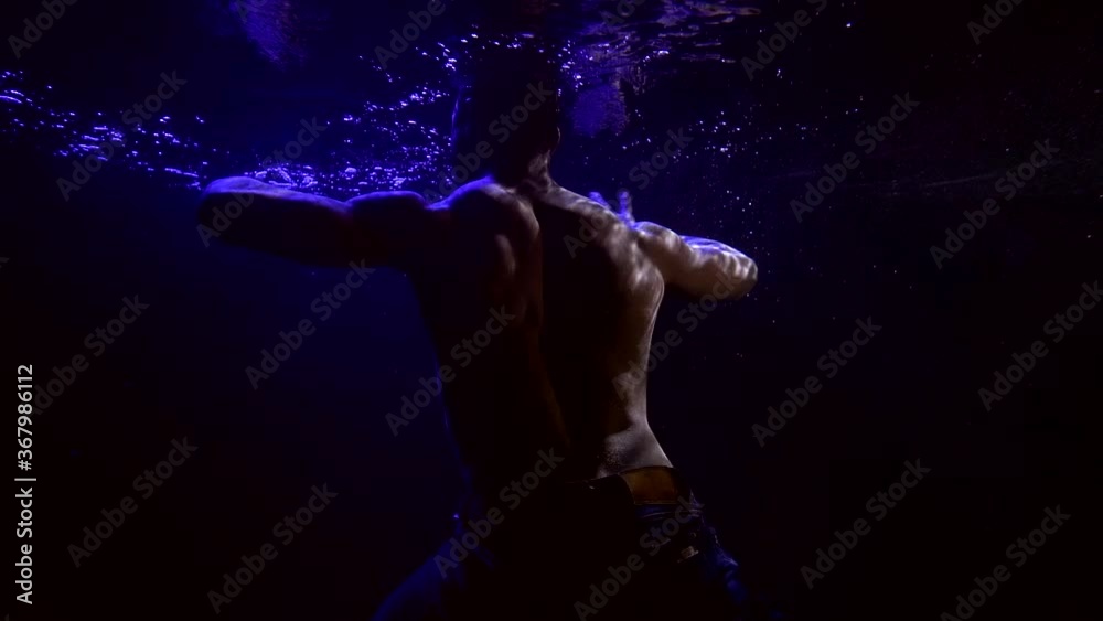 sexy man with naked muscular torso is moving underwater in darkness, dancing by hands sexy man with naked muscular torso is moving underwater in darkness, dancing by hands
