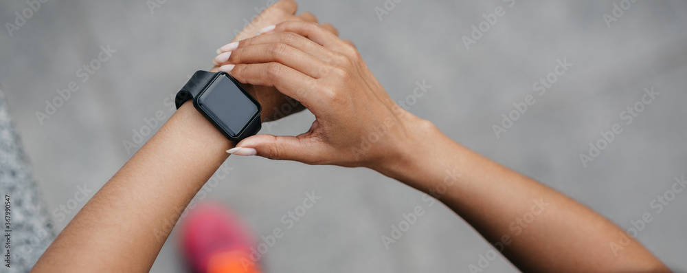 Selecting training mode. African american young woman runs on road in city and checks fitness tracker while jogging