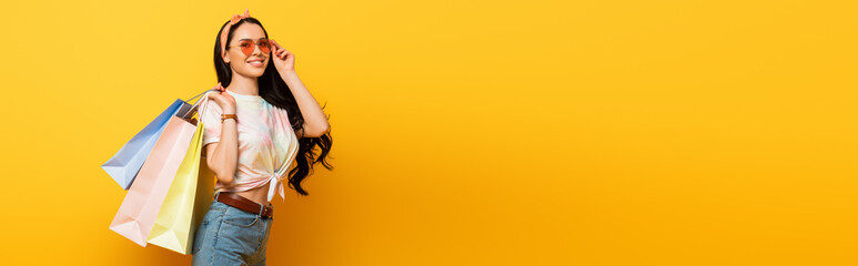 smiling stylish summer brunette girl with shopping bags on yellow background, panoramic shot