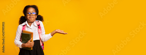 Fotografie Puzzled African American Schoolgirl Shrugging Shoulders Over Yellow Background,