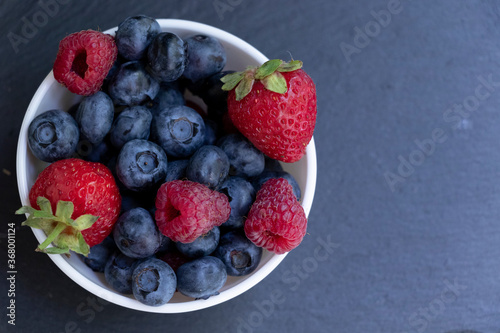 Set of summer berries in a small white bowl on a blackboard. Blueberries  raspberries  and strawberries are a varied healthy snack. Yummy.