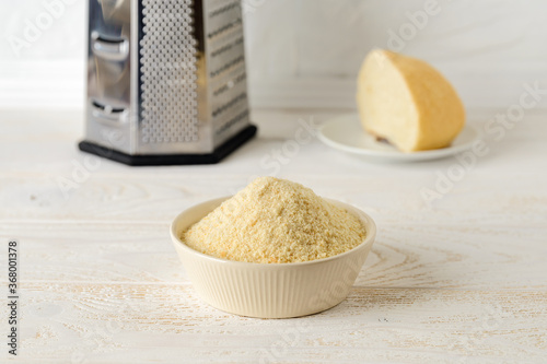 Wheat bread crumbs in a beige ceramic bowl on a kitchen table. A crust of dry bread and a grater in the background. Ingredient for meatballs and cutlets. Cook at home.