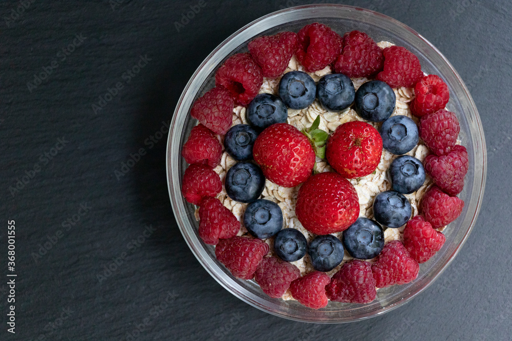 Set of summer berries with oatmeal and chia seeds in a small glass bowl on a black stone background. Perfectly healthy summer breakfast. Yummy. Set of summer berries with oatmeal and chia seeds in a small glass bowl on a black stone background. Perfectly healthy summer breakfast. Yummy.