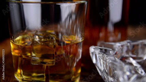 A glass of whiskey with ice cubes, a bottle and a cigar in the smoke on a wooden barrel