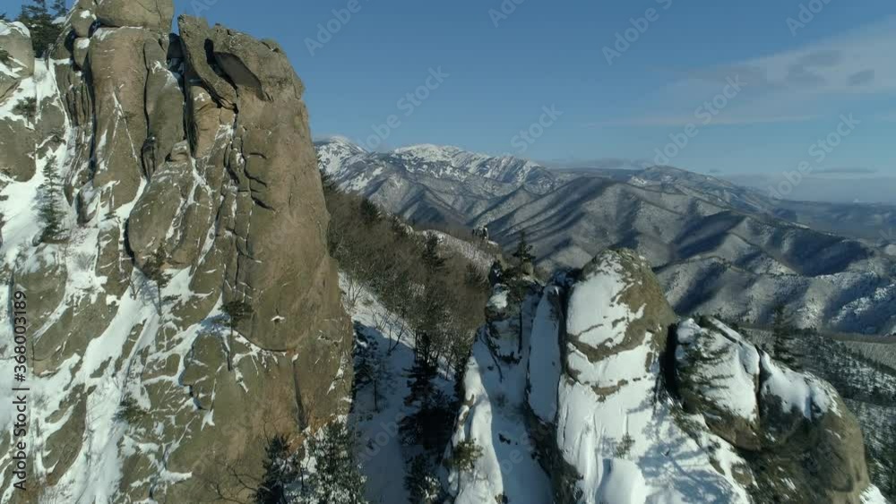 Epic rocky mountains, huge megalith stones on top covered with snow. Tree forest rock formations on slopes. Winter natural North landscape hills. unique Far East of Russia Lazo. Aerial forward