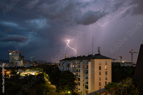 Violent summer thunderstorm with enormous lightning over the Wienerberg City in Vienna with construction cranes on the right side of the picture photo