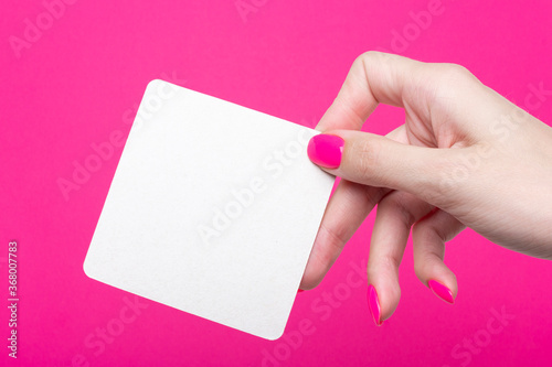 Female hand holds one square empty coasters on pink background