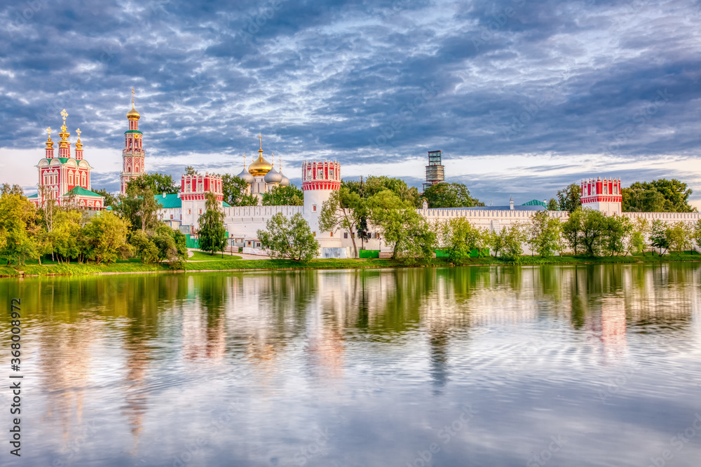 The famous Moscow landmark with Golden domes and a reflection of the landscape on the water of the Park pond against the background of a picturesque blue sky with clouds.
