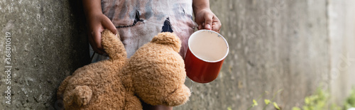 Panoramic crop of beggar african american child holding teddy bear while begging alms on urban street photo