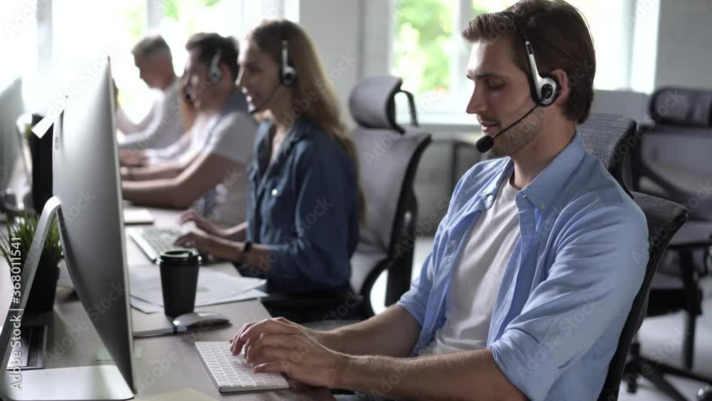 Focused male representative call center agent in wireless headset helping client with complaints using computer in office, corporate operator working in customer support service on helpline telesales