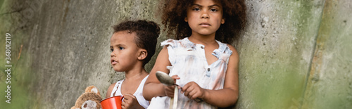 Panoramic orientation of african american kids begging alms near concrete wall in slum