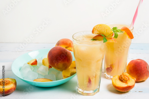 peach cold orange refreshing juice cocktail in a glass with ice and pieces of fruit and mint in the summer. top view on a light background