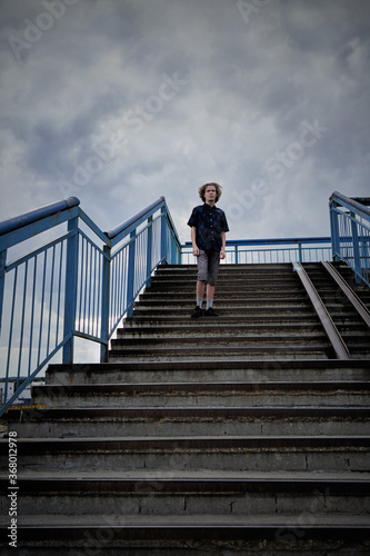 Urban teenager stands on the stairs against the backdrop of the cloudy sky. One teenager on a flight of stairs.