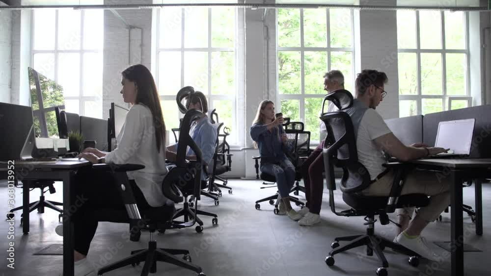 Business people office workers group using pc working talking in big modern coworking space, employees team women men sitting at desks with computers in modern enterprise interior at workplace