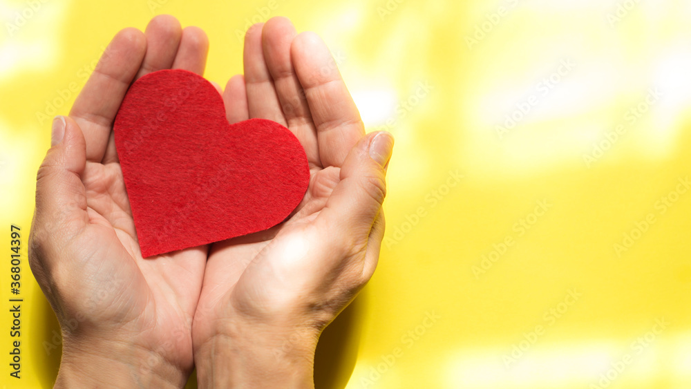 Obraz premium women's hands with a red heart on a yellow background.