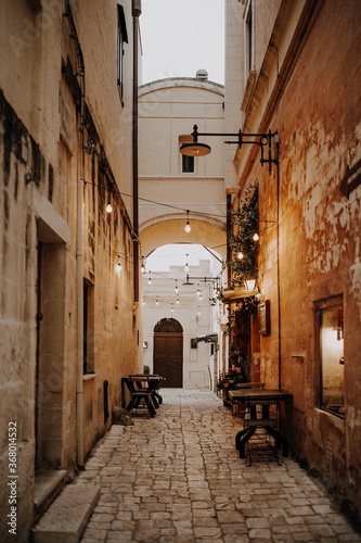 Schmale Gasse mit Lichterkette und Tischen in der Altstadt von Matera in Italien 