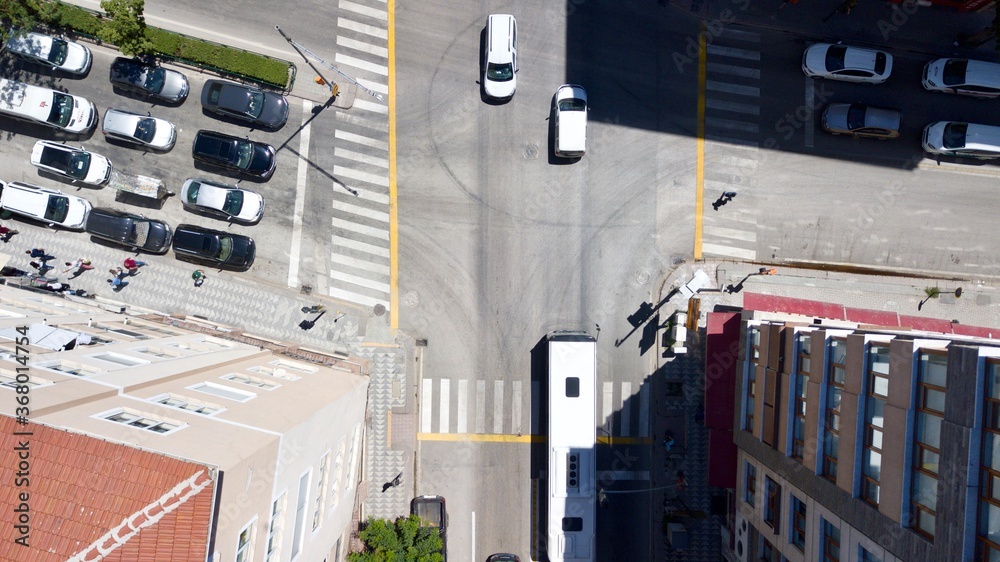 Aerial view of the crosswalk and road junction between buildings at the city center. Vehicles are waiting in red light and pedestrians are crossing the street. 